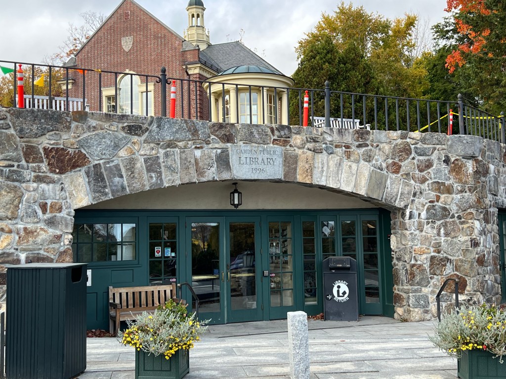 Entrance of Camden Public Library featuring a stone archway and green doors with a sign displaying the library's name and establishment year.